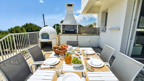 Un espacio al aire libre con comedor, una mesa dispuesta para cuatro, horno de pizza y una parrilla.