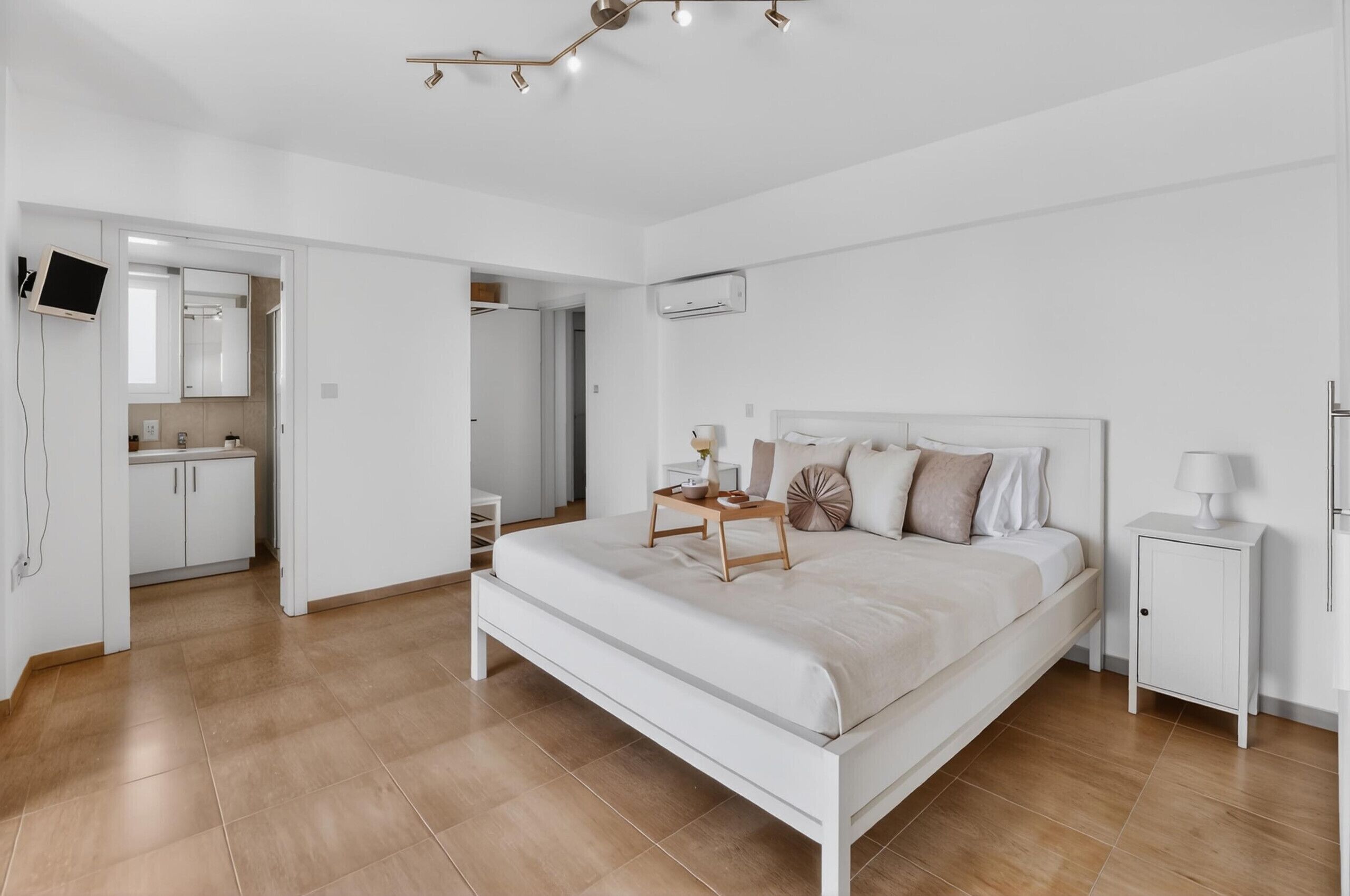A bedroom with a bed, bedside tables, a TV, and a bathroom with a mirror and sink.