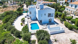 Una villa moderna con piscina, varios balcones y exuberante vegetación alrededor de la propiedad.