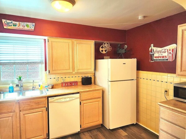 A compact kitchen with wooden cabinets, a white refrigerator, a microwave, and a sink with a window above it. - 513Company - Theater +Location (Cincinnati)