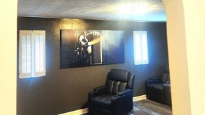 A theater room with a dark wall, a mounted screen, two windows with blinds, a black leather chair, and a wooden floor. - 513Company - Theater +Location (Cincinnati)