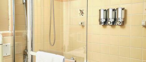 A modern bathroom with a glass-enclosed shower, a white bathtub, and beige tiled walls.