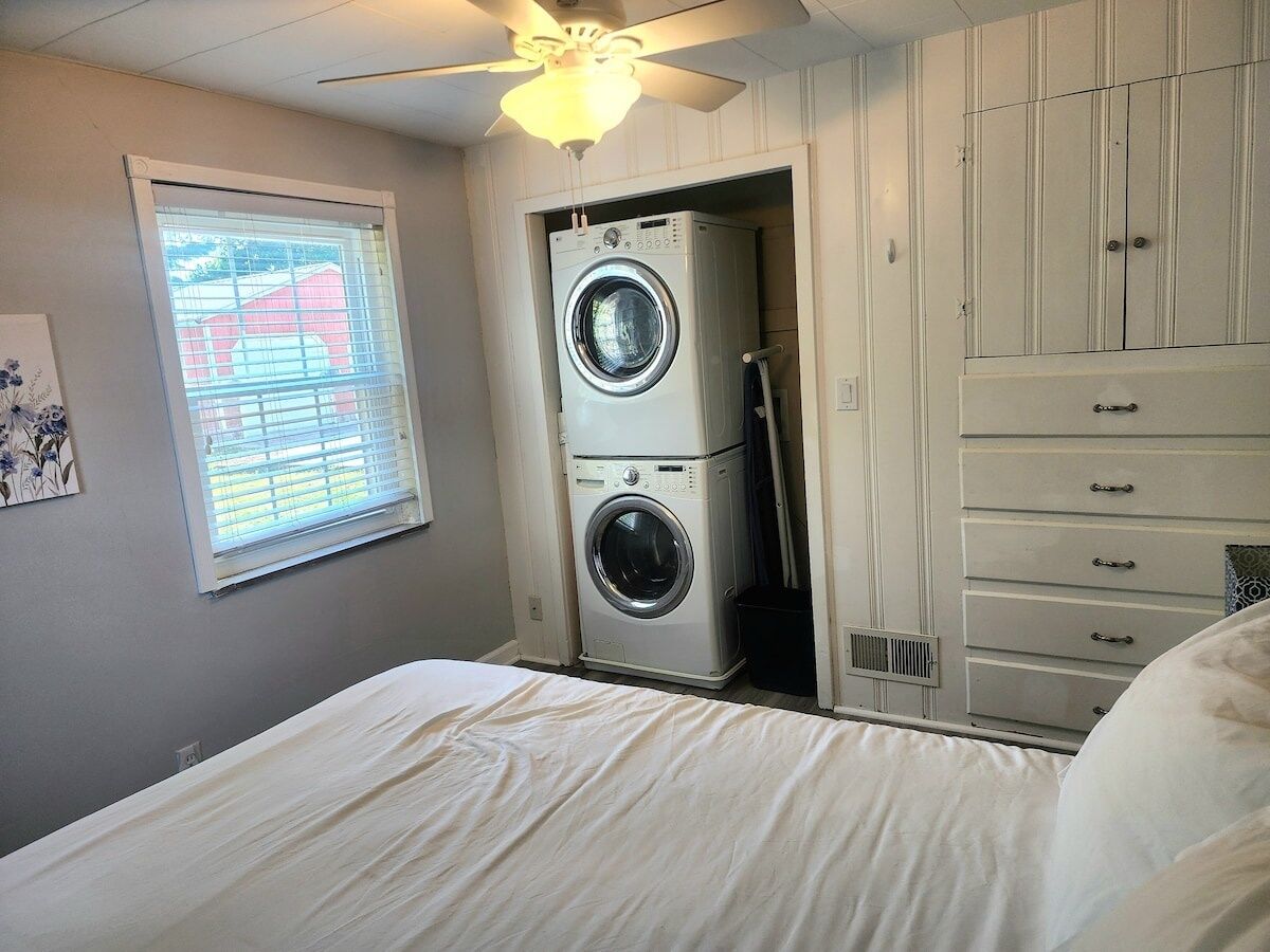 A laundry room with a front-loading washer and dryer, a ceiling fan, and a window with blinds.