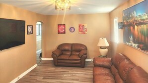 Ein Wohnzimmer mit braunem Ledersofa, einer Deckenleuchte und Wanddekorationen.