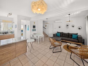 A modern living room with a sofa, two chairs, a dining table, and a kitchen area with a counter and cabinets. - Bluebell Villa Kapparis Walk to Beach (Protaras)