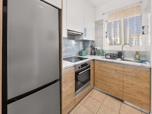 A modern kitchen with a stainless steel refrigerator, a built-in oven, and a window with patterned curtains. - Bluebell Villa Kapparis Walk to Beach (Protaras)