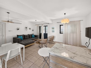 A modern living room with a sofa, chairs, a dining table, and a TV. - Bluebell Villa Kapparis Walk to Beach (Protaras)