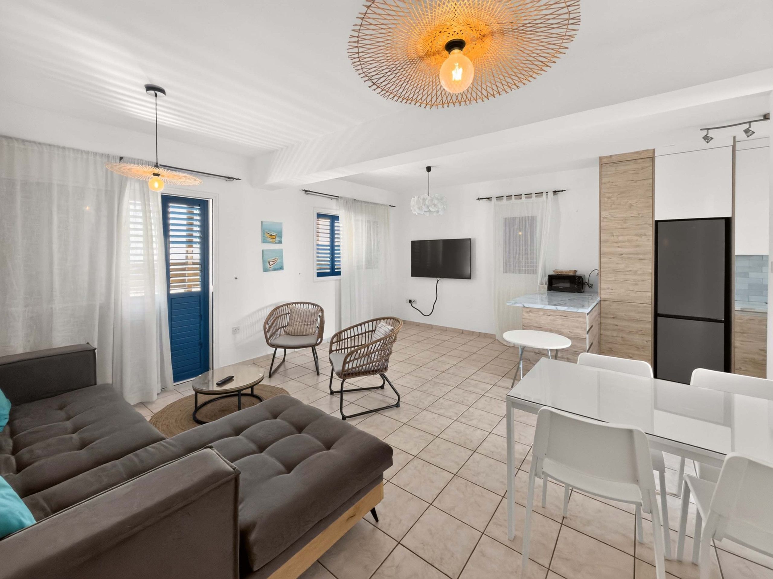 A modern living room with a sofa, chairs, a TV, and a kitchen area with a fridge and microwave.