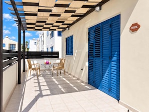 A covered outdoor seating area with a table and chairs, a blue shutter door, and a sign reading 'PERFIK'. - Bluebell Villa Kapparis Walk to Beach (Protaras)