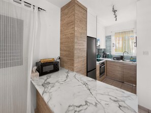 A modern kitchen with a marble countertop, wooden cabinetry, a black refrigerator, and a microwave. - Bluebell Villa Kapparis Walk to Beach (Protaras)
