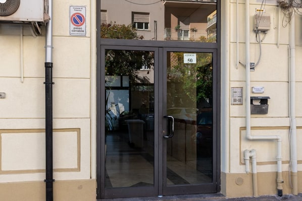 Entrada de un edificio con puerta de cristal, un cartel que dice 'Civico 50' y un letrero que indica 'passo carrabile'.