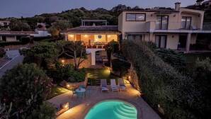 En moderne villa med swimmingpool, udendørs møbler og en velplejet have.