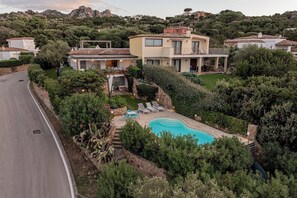 A residential area with a swimming pool surrounded by lush greenery and a road. - Villa Pitrizzina 8, Emma Villas (Sassari)