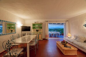 A dining area with a table and chairs, a television, and a sofa with a view. - Villa Pitrizzina 8, Emma Villas (Sassari)