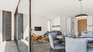 A modern dining area with a round table, grey upholstered chairs, and a contemporary pendant light. - Azure Sama Villa – Jacuzzi / Heated Pool (Protaras)