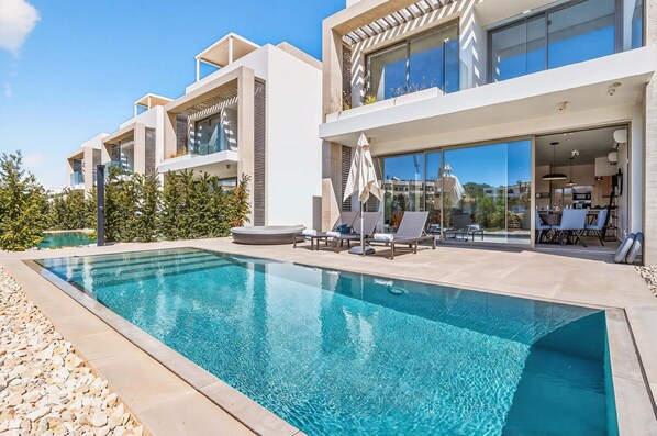 Une maison moderne dotée d’une piscine, d’un espace salon extérieur et de grandes fenêtres.