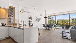 A modern kitchen with a central island, a dining area with a view, and a large window. - Azure Sama Villa – Jacuzzi / Heated Pool (Protaras)