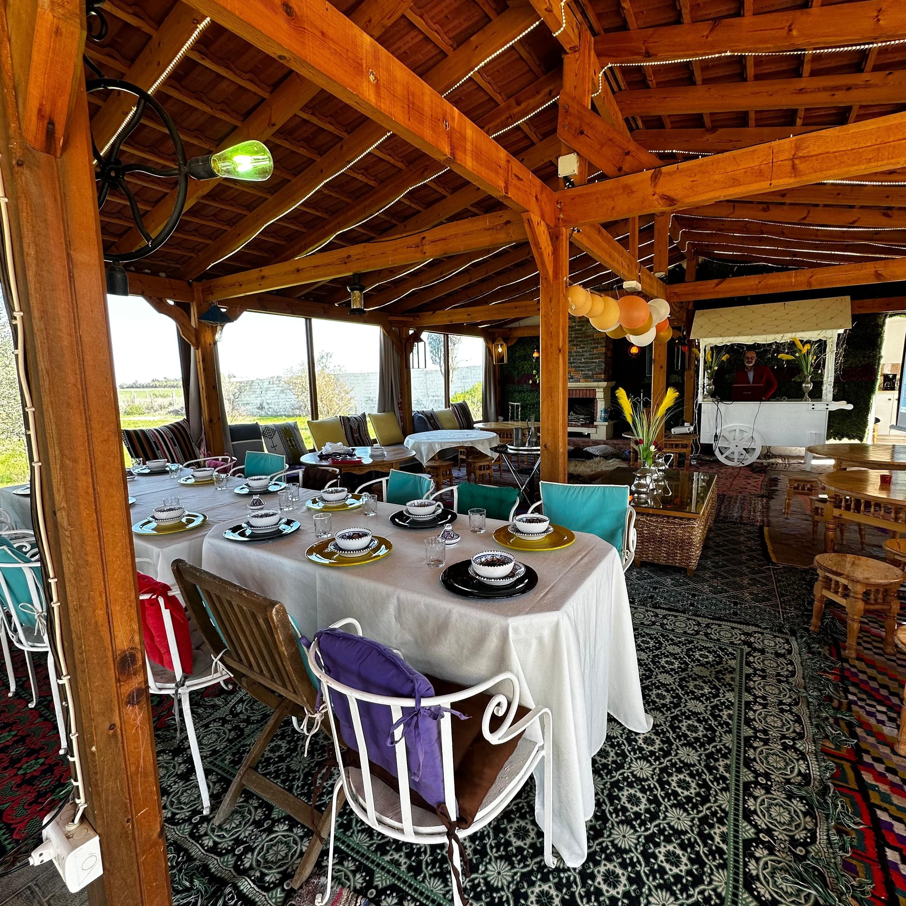 An outdoor dining area with wooden beams, tables set with plates and bowls, and chairs.