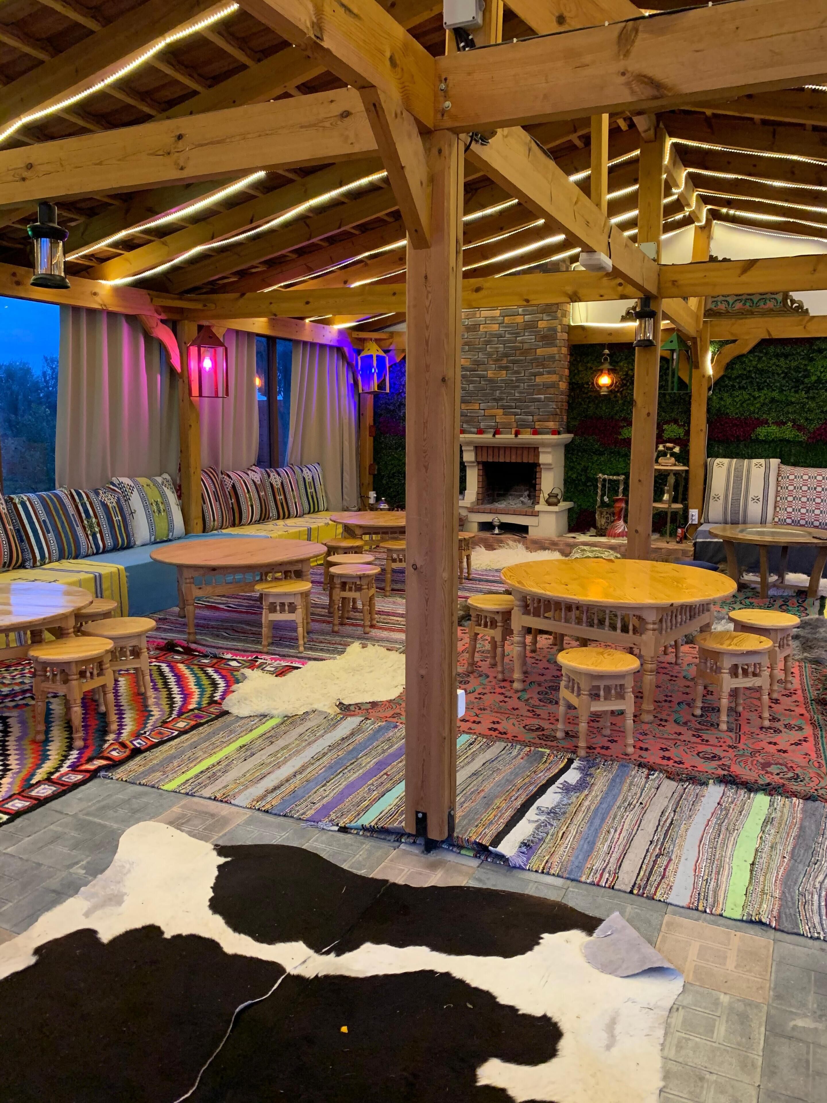 A cozy indoor seating area with wooden furniture, a stone fireplace, and a variety of colorful rugs.
