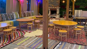 A cozy indoor seating area with wooden furniture, a stone fireplace, and a variety of colorful rugs.