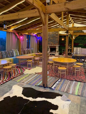 A cozy indoor seating area with wooden furniture, a stone fireplace, and a variety of colorful rugs. - Chalet Essanya (Ben Khalled)
