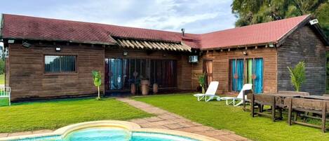 A wooden house with a swimming pool, a covered patio, and outdoor seating.
