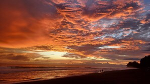 A beach with a sunset and two people walking along the shore. - Casa Pura Vista (Playa Hermosa)