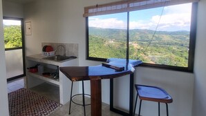 A compact kitchen with a large window offering a view of a green landscape. - Casa Pura Vista (Playa Hermosa)
