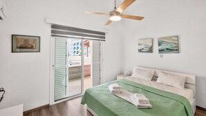 Une chambre avec une couvre-lit verte, un ventilateur de plafond et une vue sur un balcon extérieur, accessible par une porte coulissante.