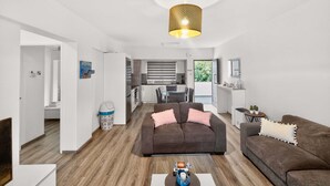Un salon moderne avec un canapé marron, une table basse blanche et une cuisine en arrière-plan.