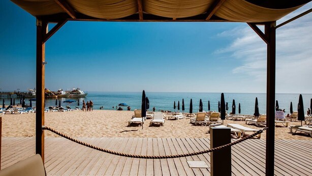 Une plage avec une terrasse en bois, des chaises longues, des parasols et une vue sur la mer.