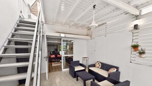 Un intérieur moderne avec un escalier, un coin salon comprenant des canapés et une table basse, et une cuisine visible à travers une porte ouverte.