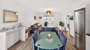 Une cuisine moderne avec un coin repas, comprenant une table centrale entourée de chaises, un réfrigérateur et une vue sur l’extérieur.