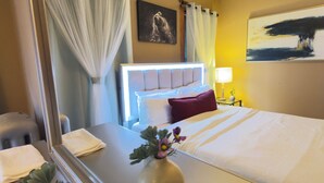 Une chambre d’hôtel avec un lit, une table de chevet ornée d’un vase de fleurs, une petite table de nuit avec une lampe et un tableau accroché au mur.