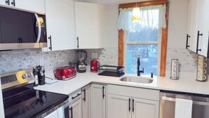 Une cuisine moderne avec des meubles blancs, une cuisinière noire, un grille-pain rouge, une machine à café et un évier.