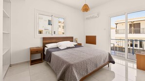 Een slaapkamer met een bed, nachtkastjes, een hanglamp, een raam en uitzicht op een balkon.