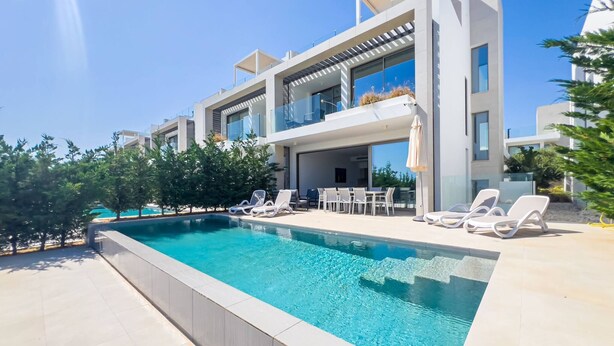 Una casa moderna de dos pisos con piscina, mobiliario exterior y un cielo azul despejado.