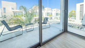 Un balcón moderno con puertas de cristal, dos sillones de descanso y una mesita.