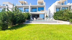 Una casa moderna de varios pisos con piscina, mobiliario exterior y abundante vegetación.