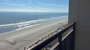 Vue sur la plage depuis un balcon doté d’une balustrade, avec l’océan et le rivage au loin.