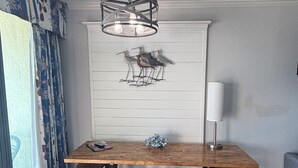 Un coin repas comprenant une table en bois, quatre tabourets, un luminaire suspendu et une œuvre d’art représentant des oiseaux, accrochée au mur.