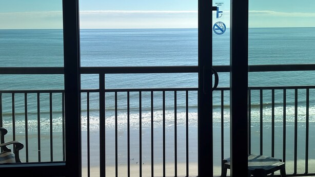 Une vue depuis un balcon doté d’une balustrade, donnant sur une plage et l’océan.