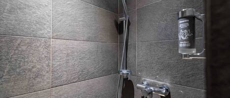 A shower with a handheld showerhead, a wall-mounted soap dispenser, and a control panel.