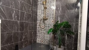 A shower area with dark marble tiles, a showerhead, and a potted plant. - Bagnol Chill - Your cosy cocoon 30 min from Avignon (4 pers.) (Bagnols-sur-Cèze)