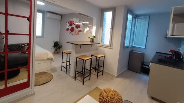 A compact living space with a kitchenette, a dining area with stools, a small seating area, and a red-framed door. - Bagnol Chill - Your cosy cocoon 30 min from Avignon (4 pers.) (Bagnols-sur-Cèze)