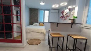 A compact bedroom with a bed, bedside tables, a window, and a red-framed door. - Bagnol Chill - Your cosy cocoon 30 min from Avignon (4 pers.) (Bagnols-sur-Cèze)