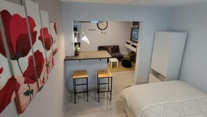 A compact room with a bed, a small kitchenette, and a dining area with two stools. - Bagnol Chill - Your cosy cocoon 30 min from Avignon (4 pers.) (Bagnols-sur-Cèze)