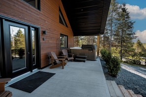 A modern building with a wooden exterior, a covered patio with seating, and a hot tub.
