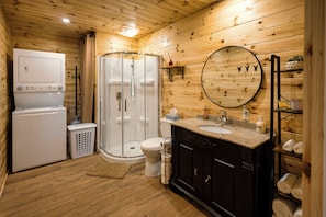 A wooden cabin bathroom with a shower, toilet, and a sink with a mirror.