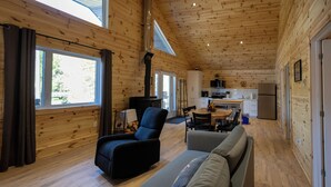 Interior de una cabaña de madera con sofá, sillón, mesa de comedor y zona de cocina.